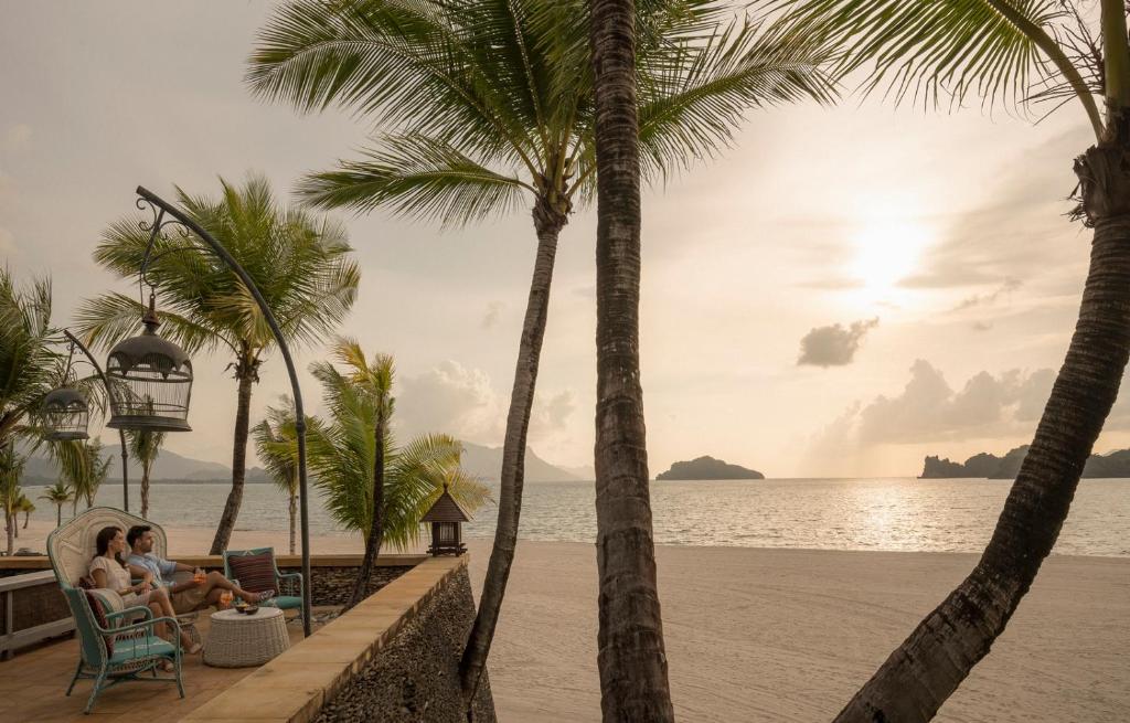two people sitting in chairs on the beach with palm trees at Four Seasons Resort Langkawi in Tanjung Rhu