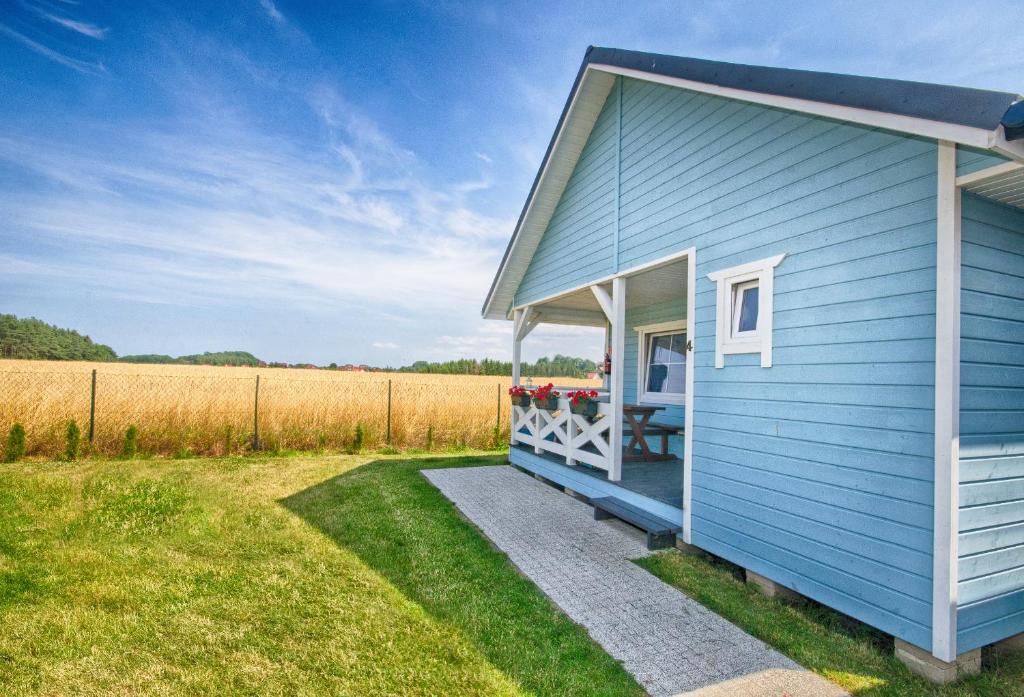 a blue house with a porch in a field at Domki PoZdrowie in Rusinowo