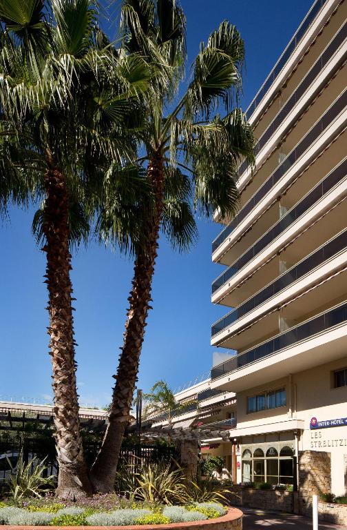 two palm trees in front of a building at The Originals Boutique, Hôtel Les Strélitzias in Juan-les-Pins