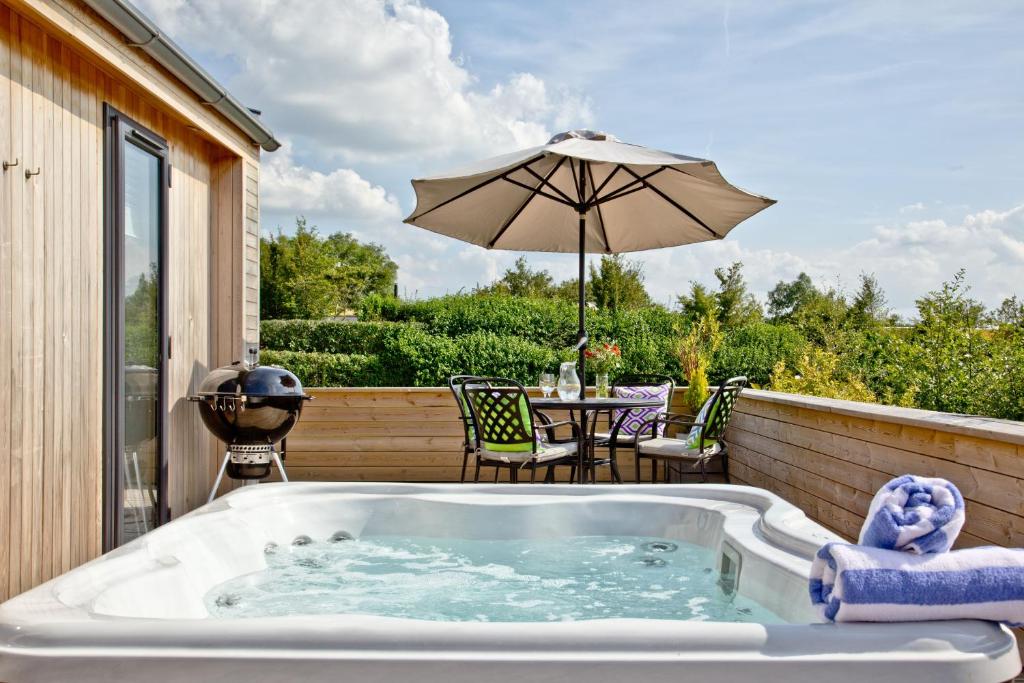 a hot tub on a patio with an umbrella at Perry Lodge, Strawberryfield Park in Cheddar