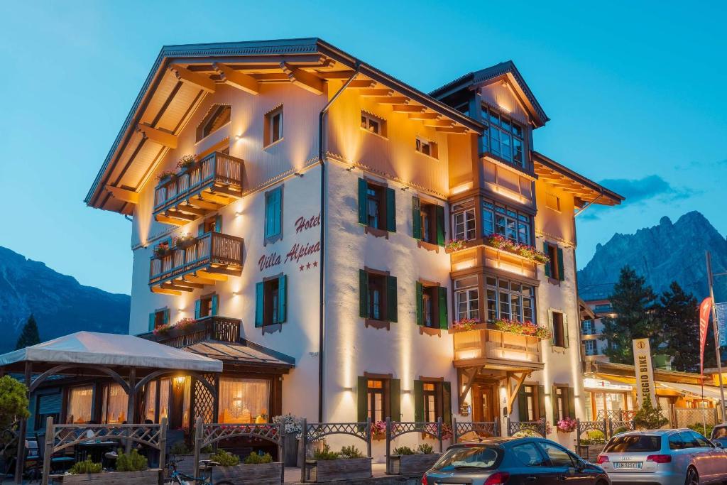 a building with cars parked in front of it at Hotel Villa Alpina ***S in Cortina dʼAmpezzo