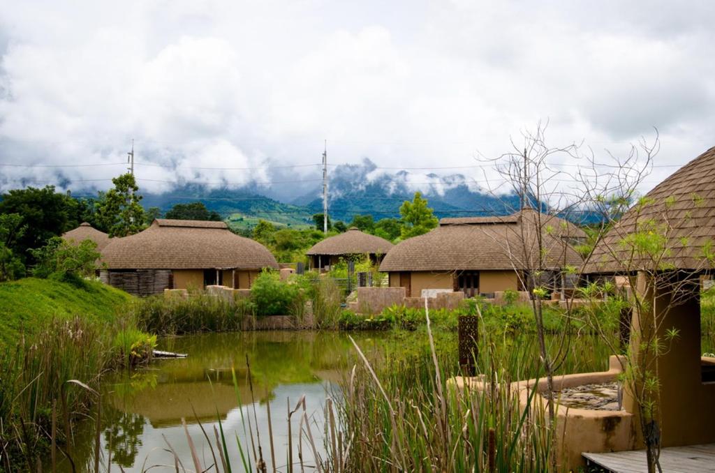 un groupe de maisons avec des montagnes en arrière-plan dans l'établissement Montis Resort, à Pai