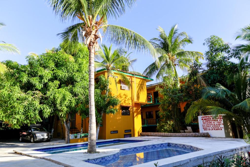 una casa amarilla con una palmera y una piscina en Hotel Posada Playa Manzanillo en Puerto Escondido