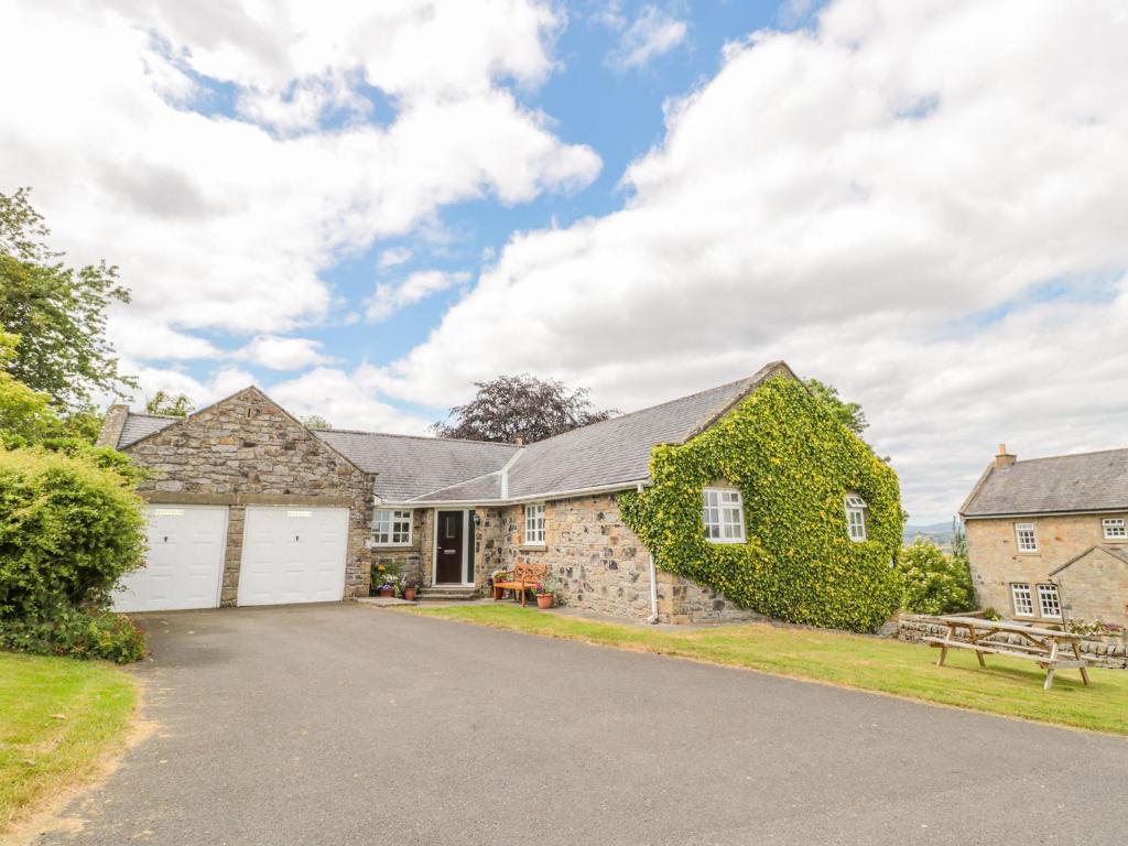 a stone house with a garage and a bench at Coquet View Cottage in Morpeth