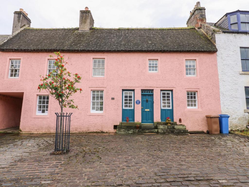 a pink house with blue doors on a cobblestone street at Shortbread Cottage in Cupar