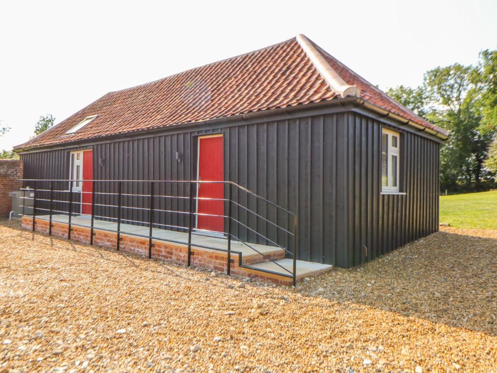 a black building with a red door and a gate at Sparrow Barn in Norwich