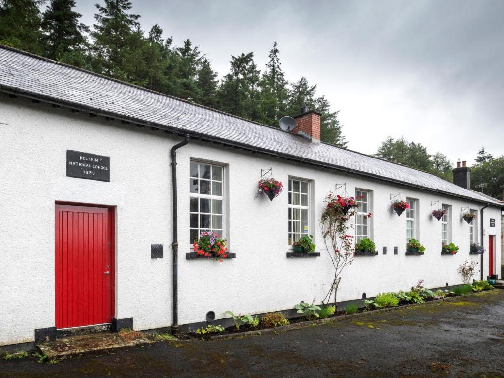 a white building with a red door and windows at The Old School in Omagh