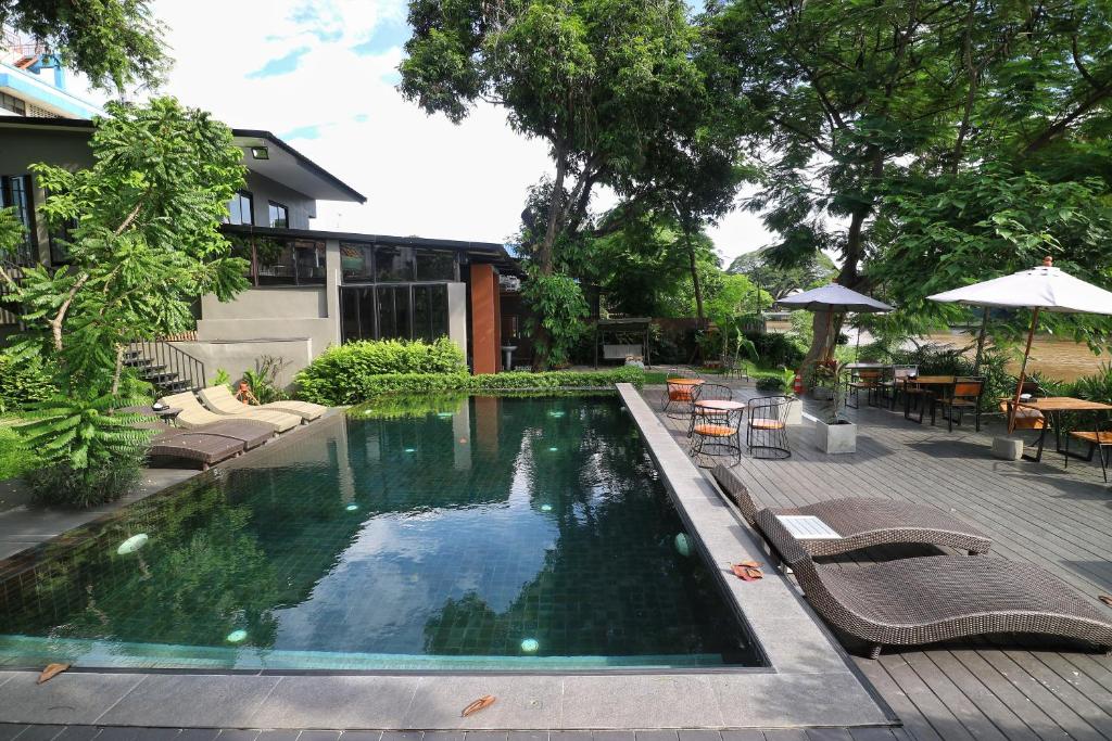a swimming pool in a yard with chairs and an umbrella at i-river chiangmai in Chiang Mai