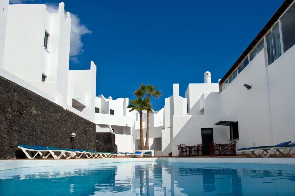 a swimming pool in front of a white building at Apartamentos Tabaiba in Costa Teguise