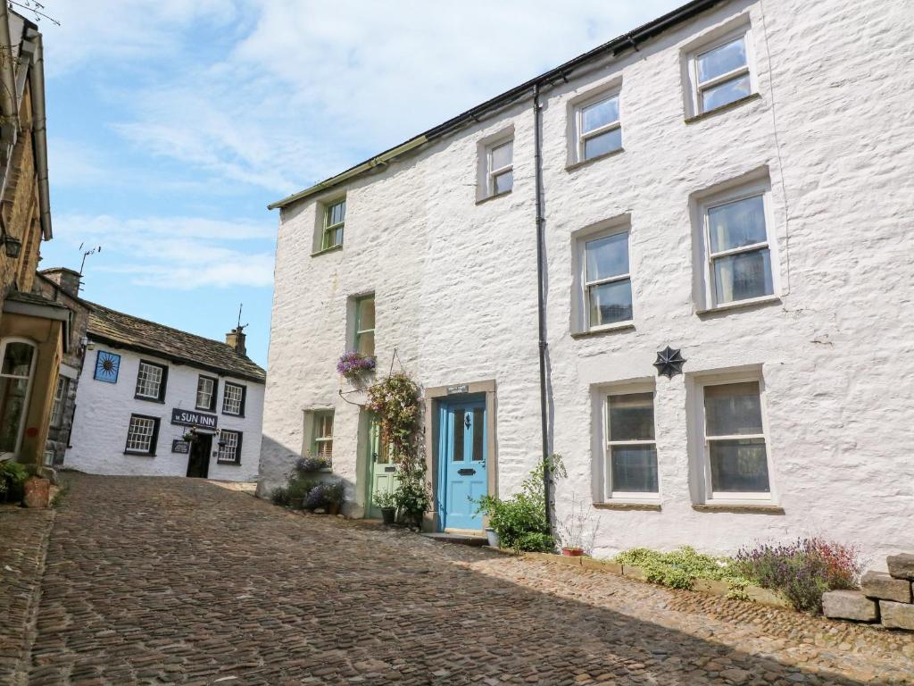 a white building with a blue door on a cobblestone street at White Hart House in Dent