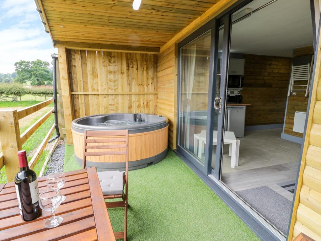 een terras met een hot tub en een tafel met een fles wijn bij Cilan Lodge in Corwen