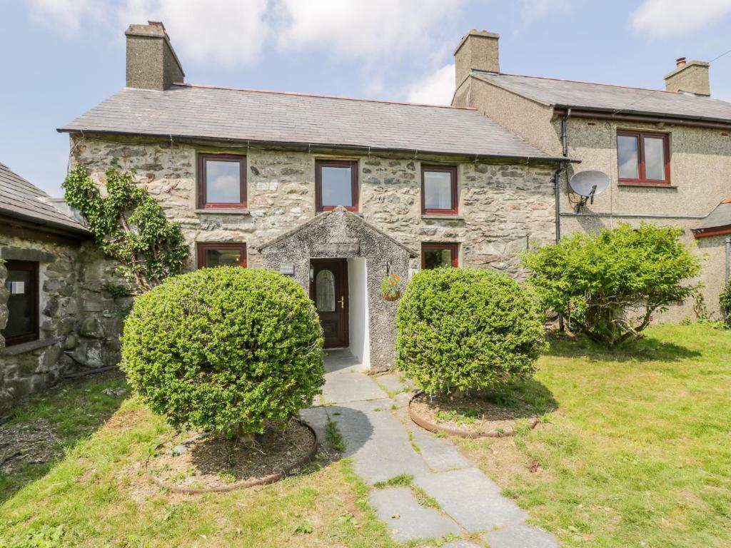 an old stone house with bushes in front of it at Bwthyn Pennant in Llanfihangel-y-pennant