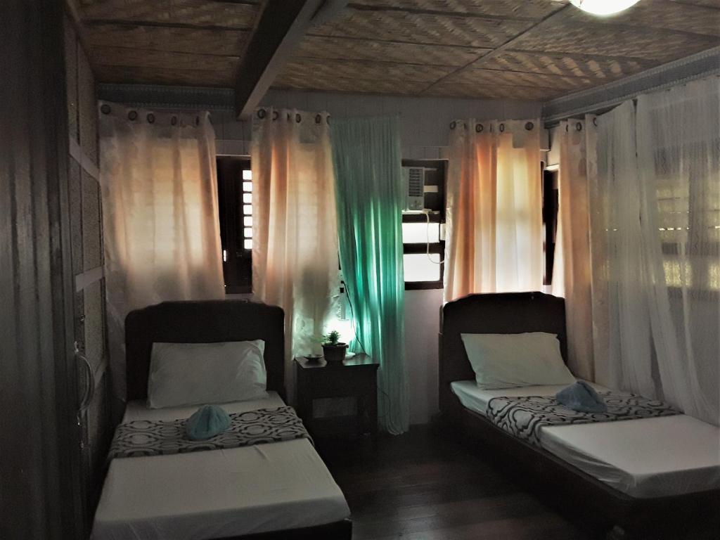 2 letti in una camera con finestre e tende di Oasis Balili Heritage Lodge a Città di Tagbilaran
