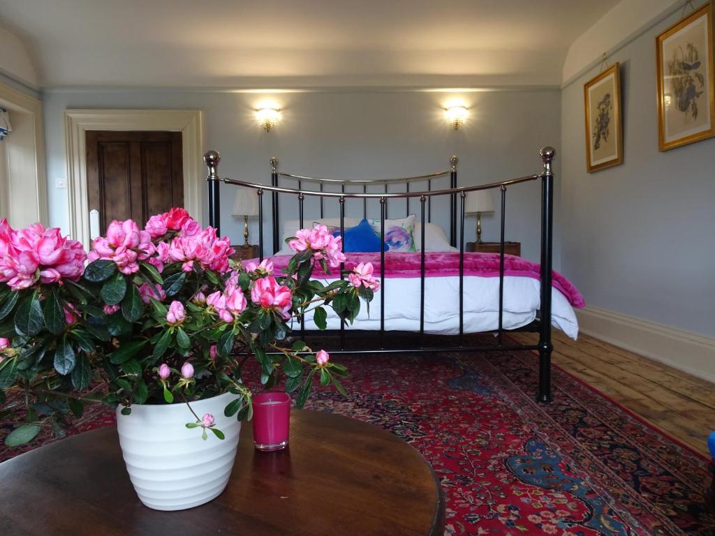 Redlynch Lodge في Redlynch: غرفة نوم مع سرير مع زهور وردية على طاولة