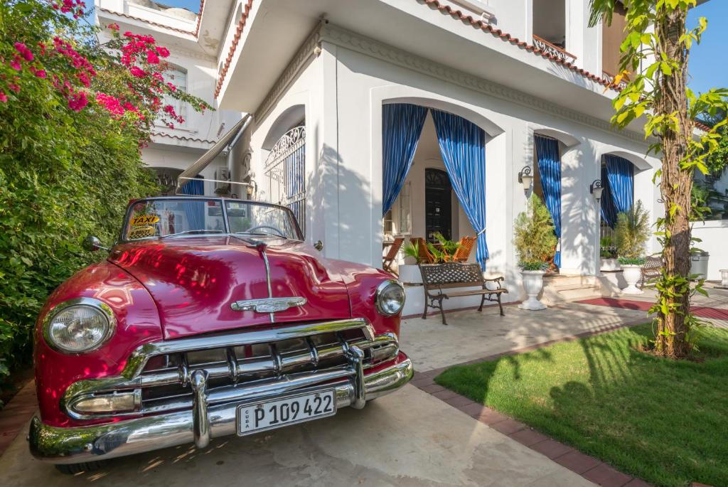 an old red car parked in front of a house at El Candil Boutique Hotel in Havana