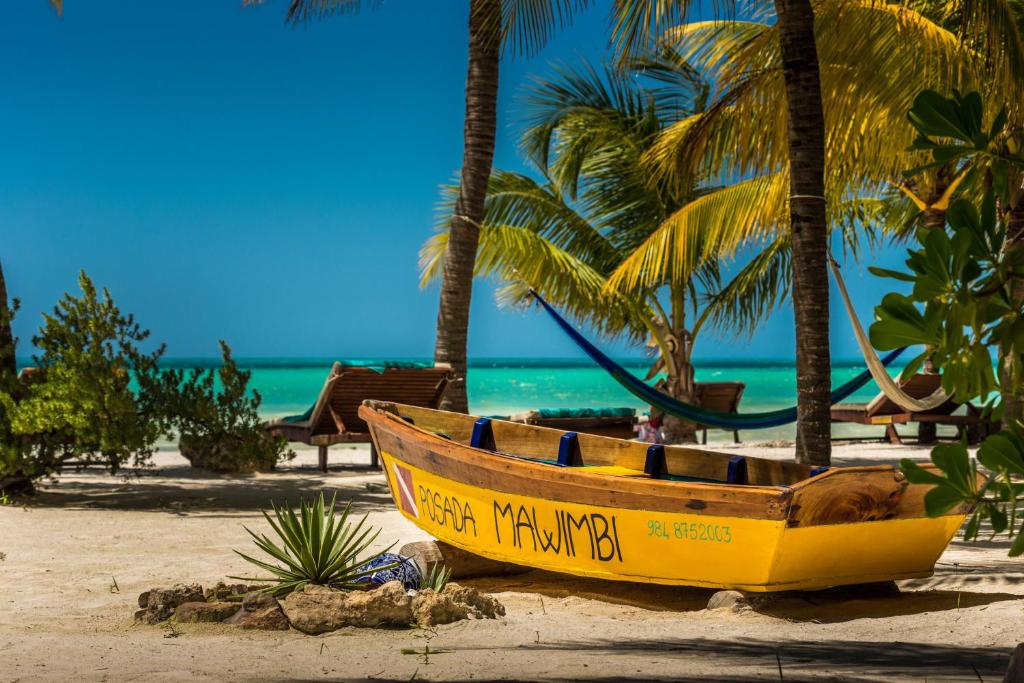 een gele boot op een strand met palmbomen bij Hotel Mawimbi in Holbox Island