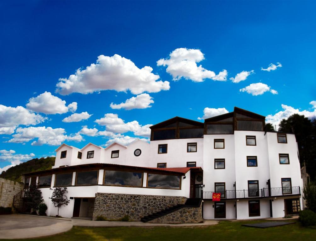 a large white building with a blue sky and clouds at Hotel Santiurde SOLO ADULTOS in Mineral del Monte