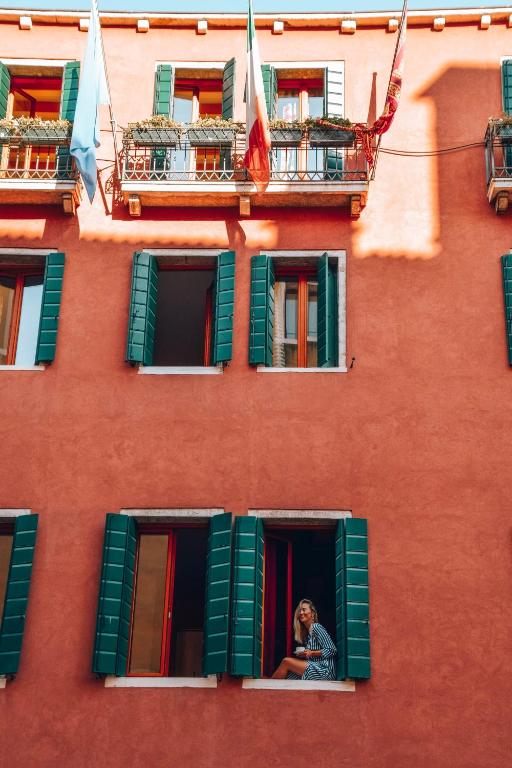 a woman looking out the window of a red building at Palazzo San Luca in Venice