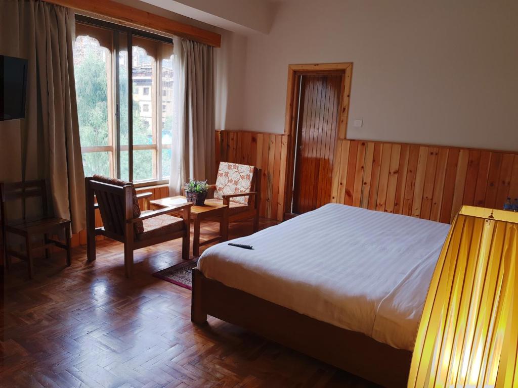 a bedroom with a bed and a chair and a window at Khamsum Inn in Thimphu