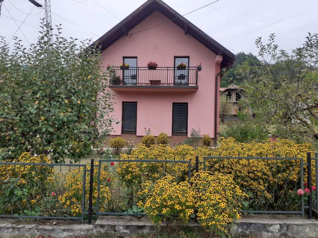 a pink house behind a fence with flowers at Rooms Violeta in Mokra Gora