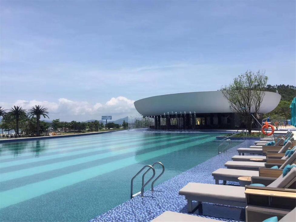 une piscine avec des chaises longues et un bâtiment dans l'établissement 惠东巽寮湾无敌海景公寓, à Huidong