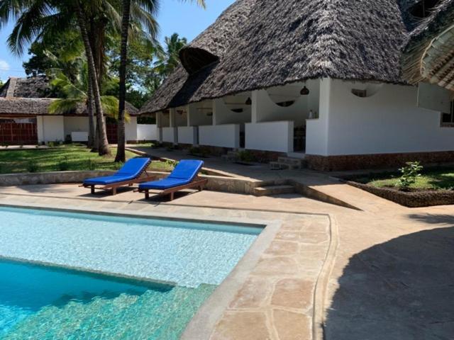 una piscina con 2 sillas azules junto a una casa en peeKAboo Diani Beach, en Diani Beach