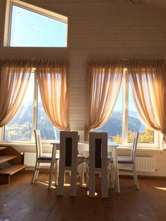 ein Esszimmer mit einem Tisch, Stühlen und Fenstern in der Unterkunft Котедж Аквамарин in Jaremtsche