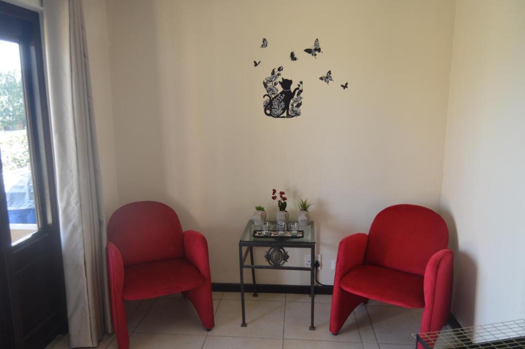 two red chairs and a table with a clock on the wall at Oppidam Self Catering Accommodation in Clanwilliam