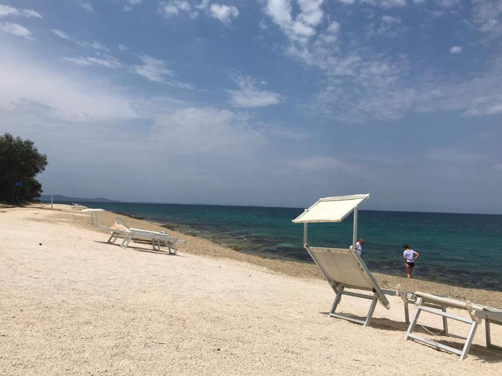a beach with two chairs and a white umbrella at Nikola Luxury Apartments Senia in Petrcane
