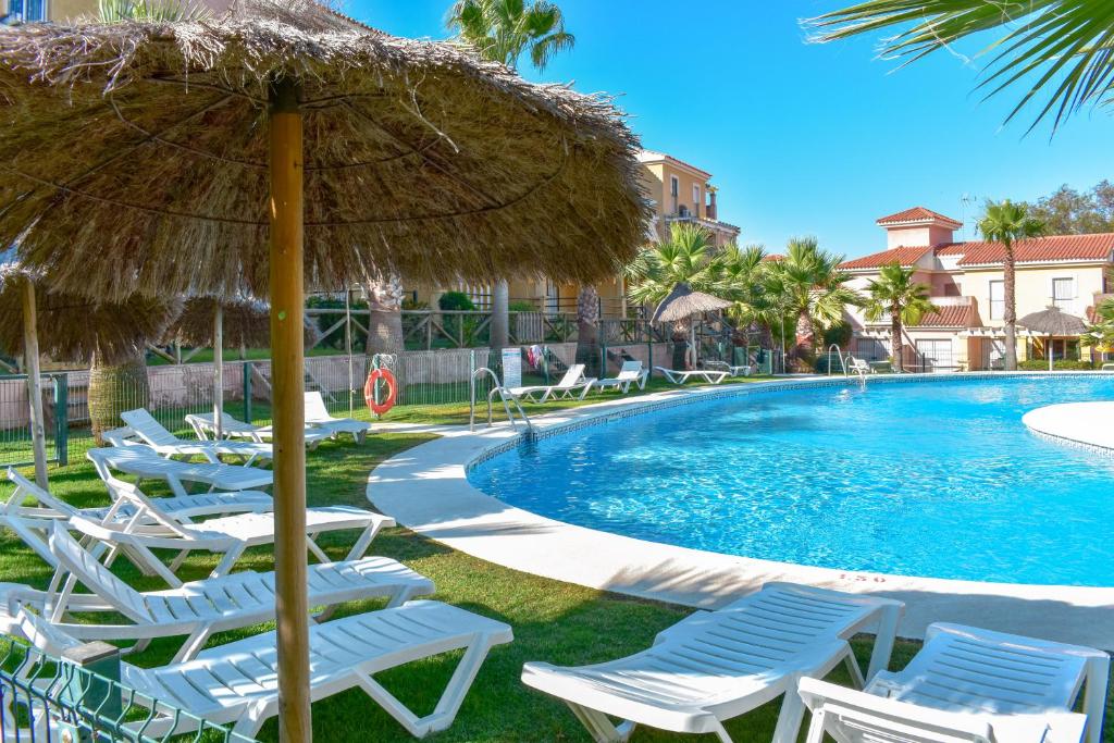 un grupo de sillas y una piscina con sombrilla de paja en Disfrute de las playas y el golf en nuestro adosado en Islantilla - Costa de la Luz, en Lepe