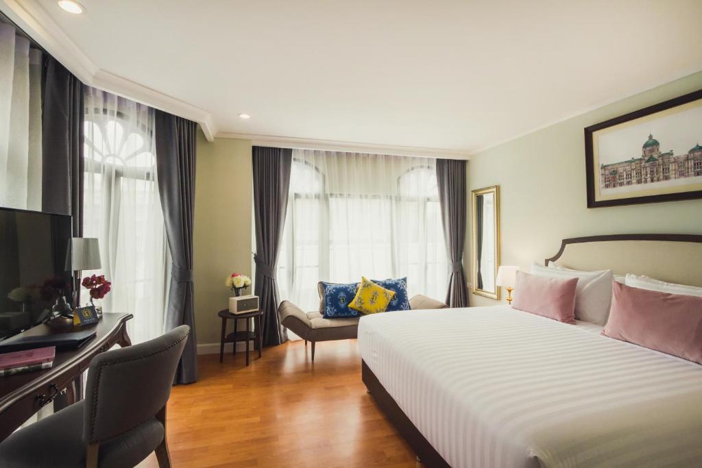 A bright guest room with a large bed, desk, television and curtained windows.