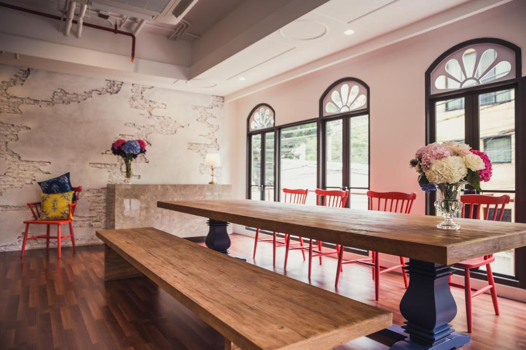 A bright communal dining room with a long wooden table and red chairs.