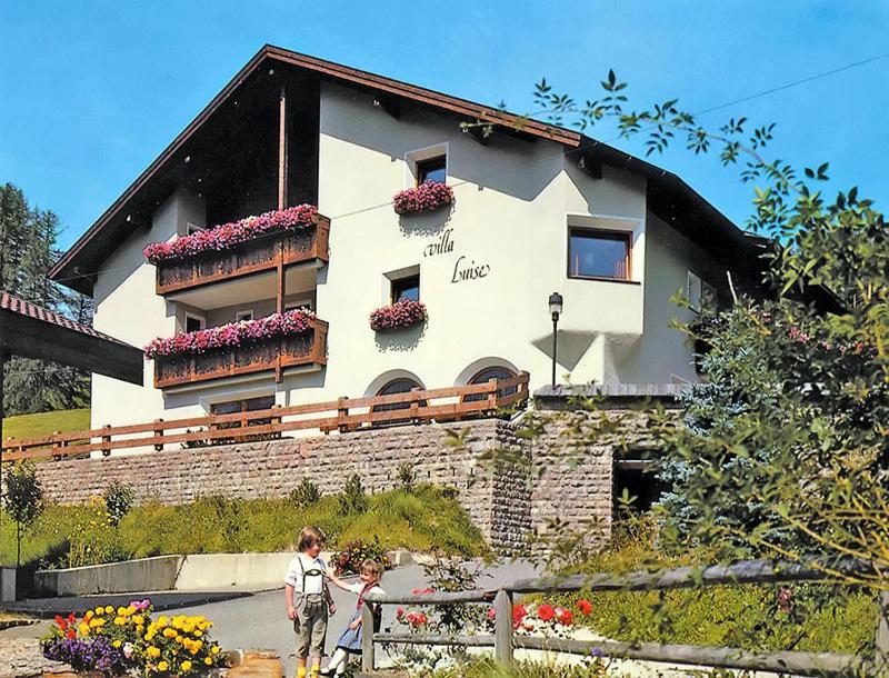 dos personas caminando frente a un edificio con flores en Villa Luise en Ortisei