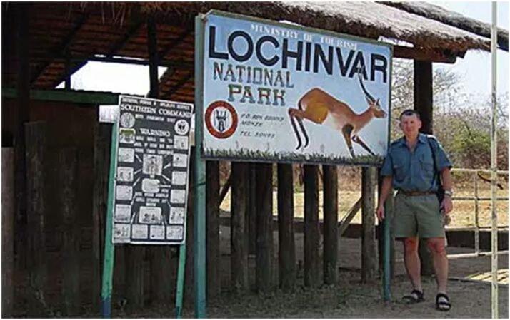Lochinvar Safari Lodge of Lochinvar National Park - ZAMBIA في Lochinvar National Park: رجل واقف بجانب لافته عليها الكنغر
