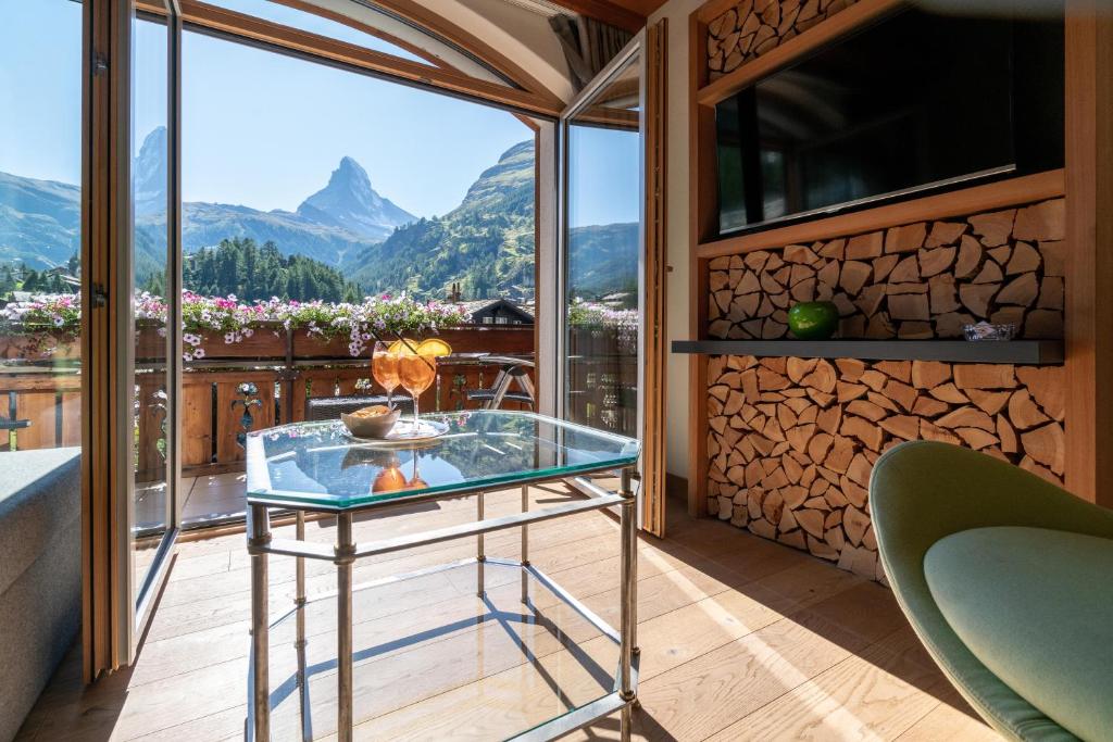 a glass table on a balcony with a view of mountains at Hotel Eden Wellness in Zermatt