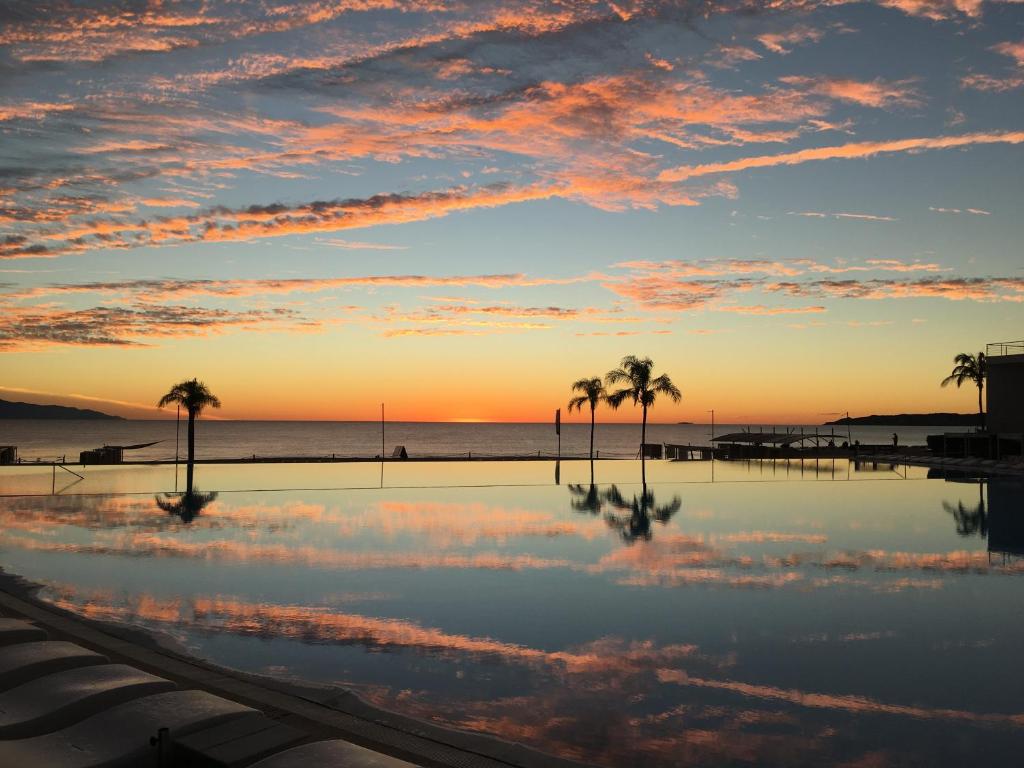 - une piscine avec des palmiers et l'océan au coucher du soleil dans l'établissement Estudio 310 Nuevo Vallarta, frente al mar, totalmente equipado y amueblado!, à Nuevo Vallarta