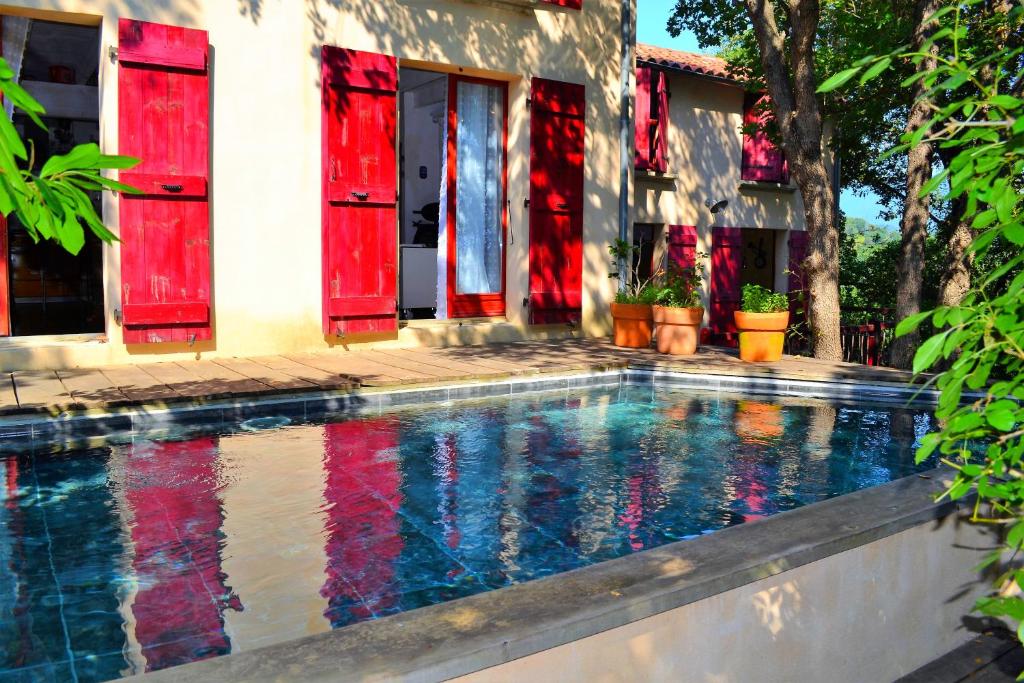 a swimming pool in front of a house with red windows at Maison de la Vigne in Venzolasca