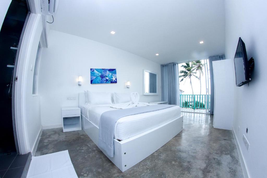 a white bedroom with a large bed and a television at Somerset Mirissa Beach in Mirissa