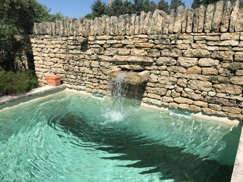 een zwembad met een stenen muur en water bij Le Moulin des Sources in Gordes