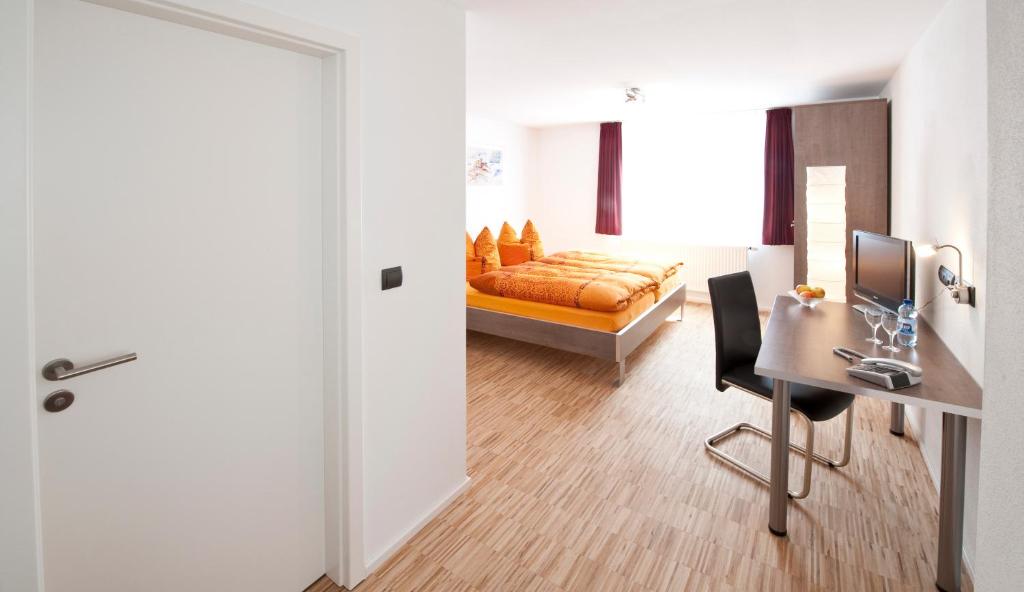 a bedroom with a bed and a desk and a door at Hotel Merlin in Filderstadt