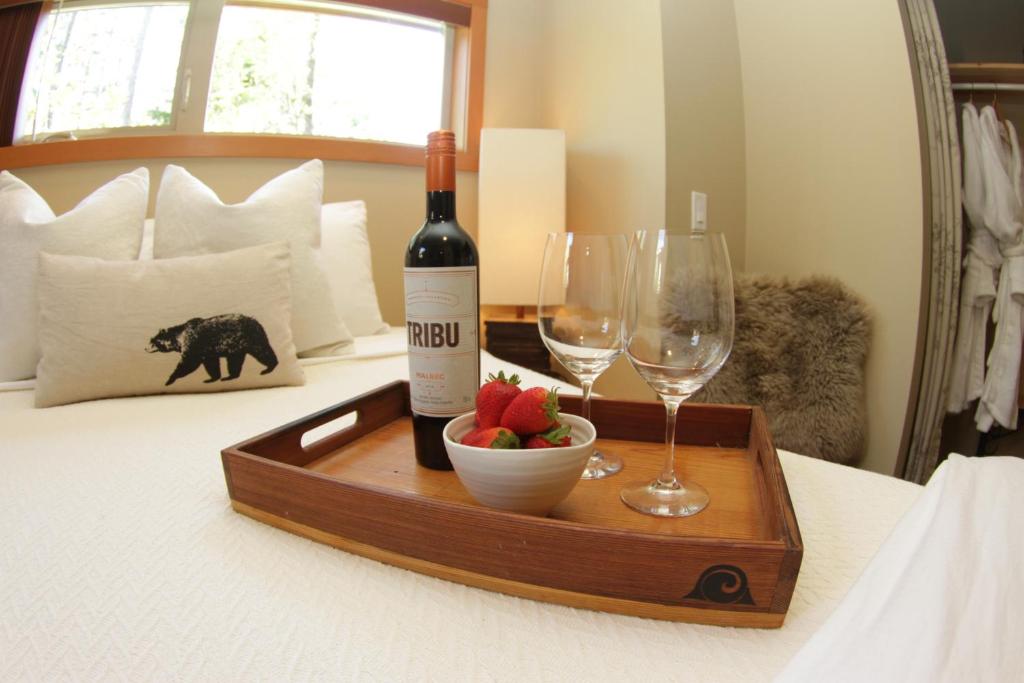 a bottle of wine and a bowl of fruit and wine glasses on a bed at Black Bear Guesthouse in Tofino