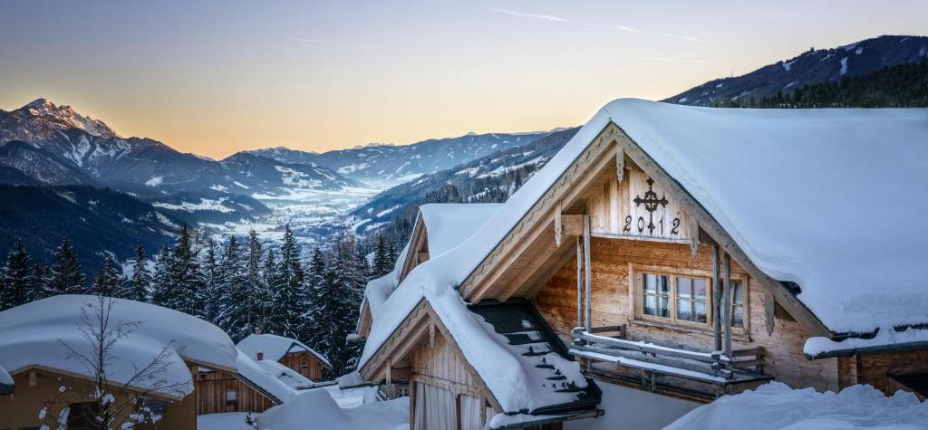 a log cabin covered in snow with mountains in the background at Almdorf Reiteralm in Schladming