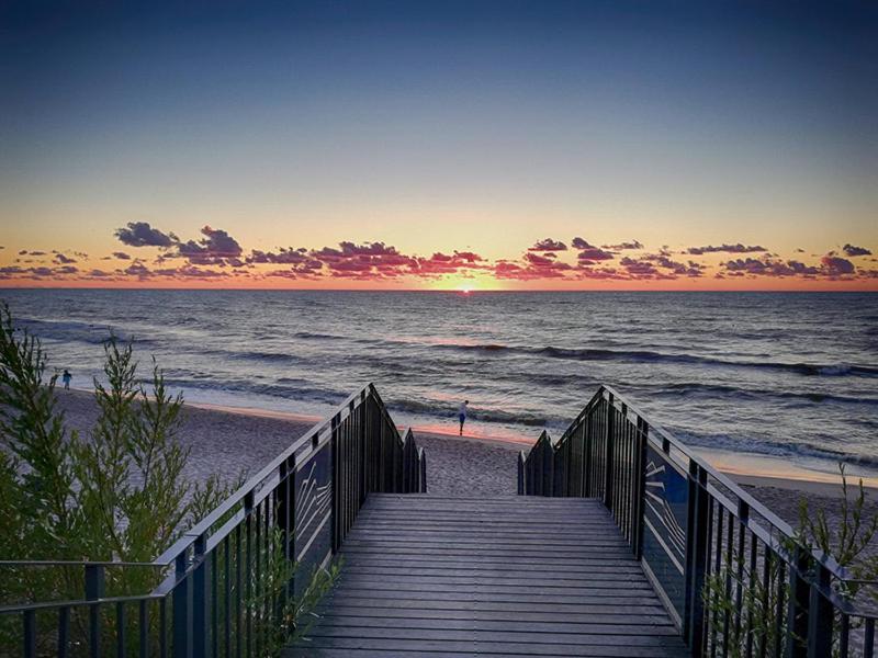 un paseo marítimo de madera que conduce a la playa al atardecer en Apartament Sosnowa 13, en Mielno