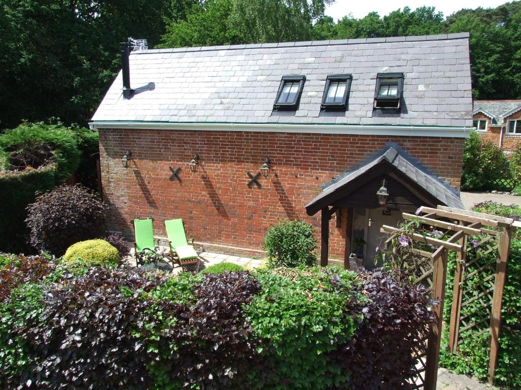 a brick house with two green chairs in a garden at The Barn in Redlynch