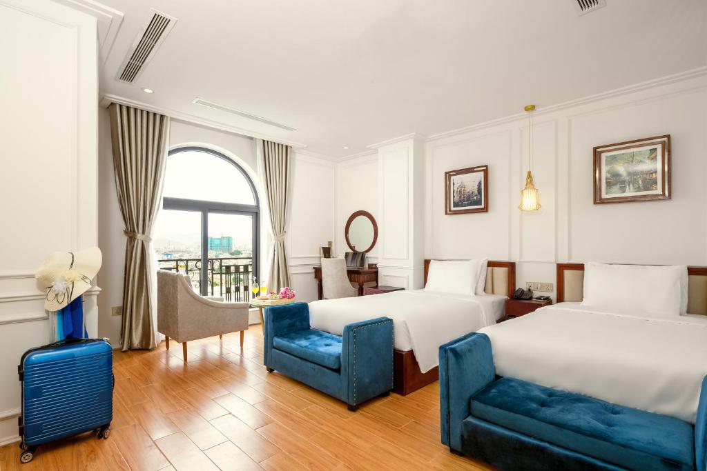 a hotel room with two beds and a blue chair at Menora Grand Da Nang in Da Nang