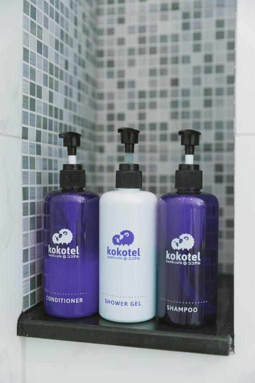 Three branded pump bottles sit on a shelf in a tiled shower area.
