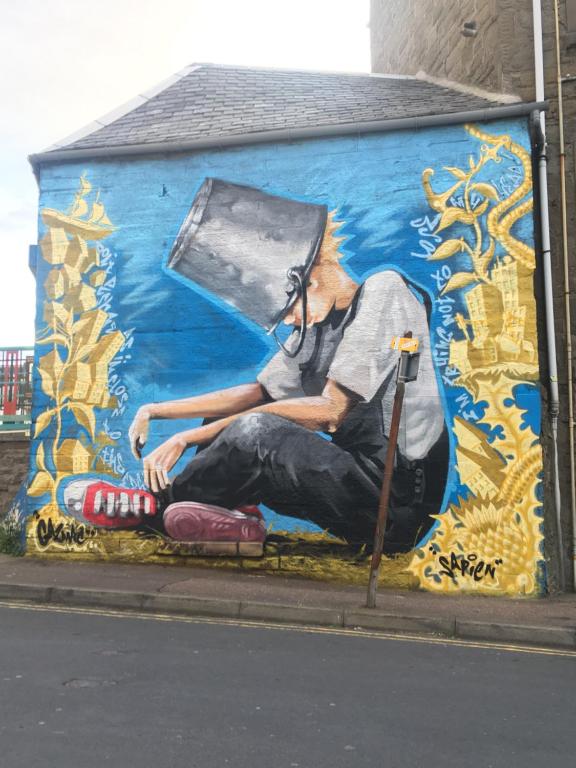 a painting of a man sitting on the side of a wall at Bank Street Gallery in Kirriemuir