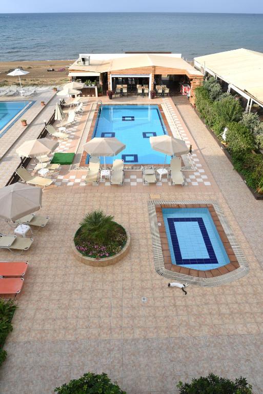 a swimming pool with umbrellas and chairs and the ocean at Esperides Beach Hotel Apartments in Stalos