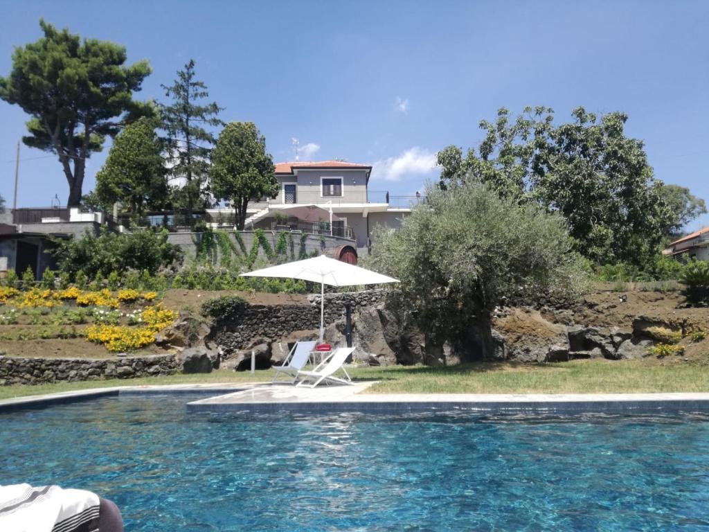 una silla blanca y una sombrilla junto a la piscina en Casa di Sara en Zafferana Etnea