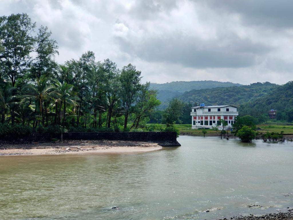 a white house on the side of a river with a building at Shobha Farmhouse in Kashid